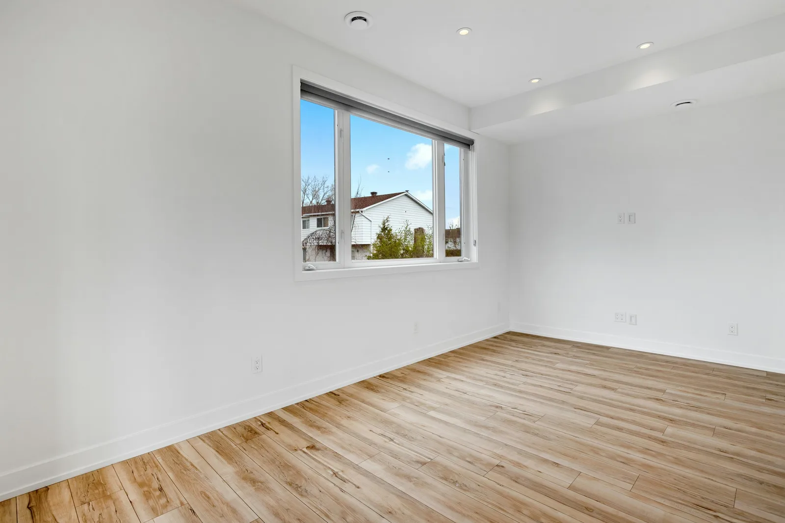 Empty freshly turned rental room with wood floors and a window view of a suburban house